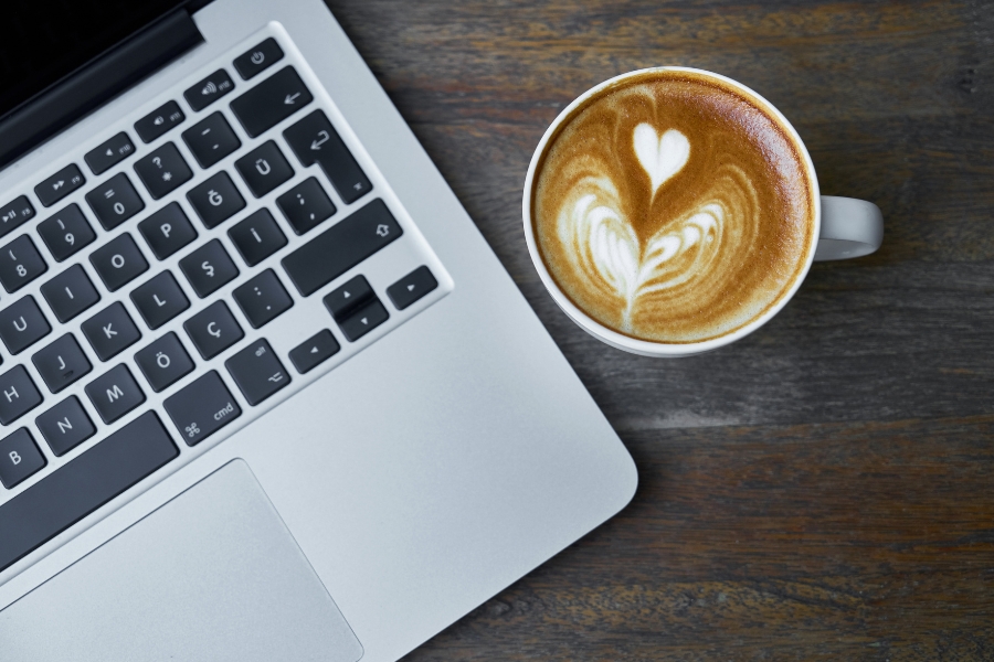 מבט עילי על מחשב נייד ולידו כוס קפה המונחים על שולחן שחור.